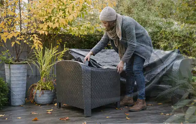 Person deckt Gartenmöbel vor der kalten Jahreszeit sorgfältig ab; Thema Outdoor Küchen, Schwerpunkt Fehlerhilfe; Praxisalltag.