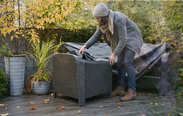 Person deckt Gartenmöbel vor der kalten Jahreszeit sorgfältig ab; Thema Outdoor Küchen, Schwerpunkt Testkriterien; Praxisalltag.