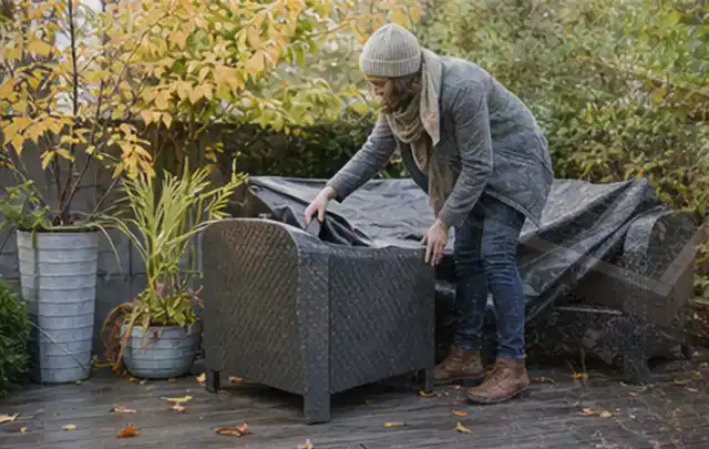 Person deckt Gartenmöbel vor der kalten Jahreszeit sorgfältig ab; Thema Outdoor Küchen, Schwerpunkt Vergleich; Ausgangslage.