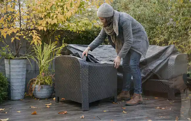 Person deckt Gartenmöbel vor der kalten Jahreszeit sorgfältig ab; Thema Pelletgrills, Schwerpunkt Dimensionierung; Ausgangslage.