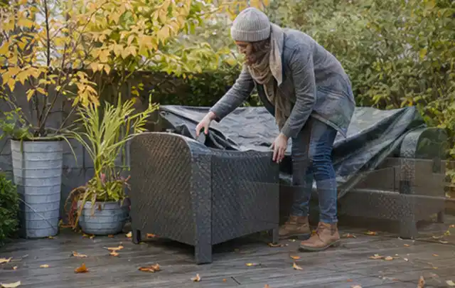 Person deckt Gartenmöbel vor der kalten Jahreszeit sorgfältig ab; Thema Pelletgrills, Schwerpunkt Fehlerhilfe; Ausgangslage.