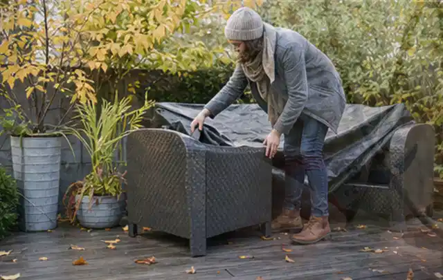 Person deckt Gartenmöbel vor der kalten Jahreszeit sorgfältig ab; Thema Pelletgrills, Schwerpunkt Systemvergleich; Umsetzung.
