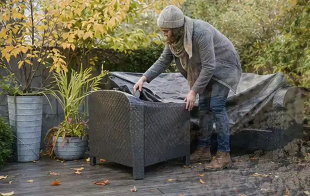 Person deckt Gartenmöbel vor der kalten Jahreszeit sorgfältig ab; Thema Pelletgrills, Schwerpunkt Testkriterien; Praxisalltag.