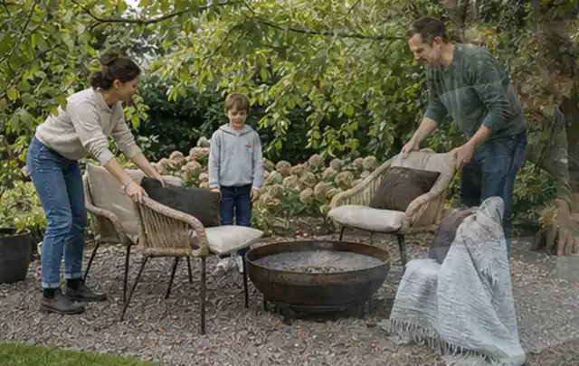Familie stellt wetterfeste Sessel an einem geschützten Sitzplatz im Garten auf; Thema Pelletgrills, Schwerpunkt Wartung; Umsetzung.