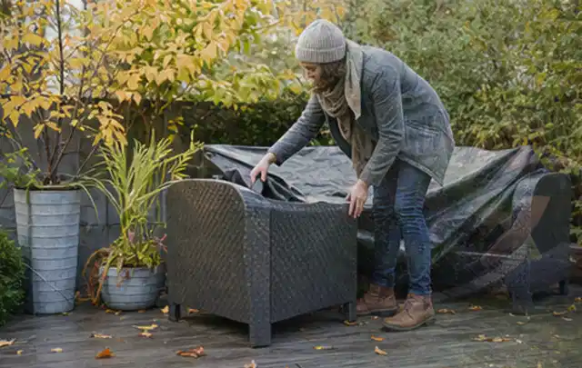 Person deckt Gartenmöbel vor der kalten Jahreszeit sorgfältig ab; Thema Pelletgrills, Schwerpunkt Wartung; Praxisalltag.