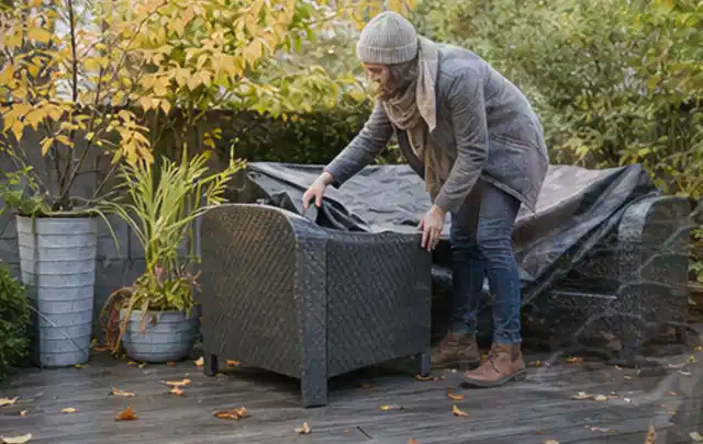 Person deckt Gartenmöbel vor der kalten Jahreszeit sorgfältig ab; Thema Pelletgrills, Schwerpunkt Winterlager; Umsetzung.