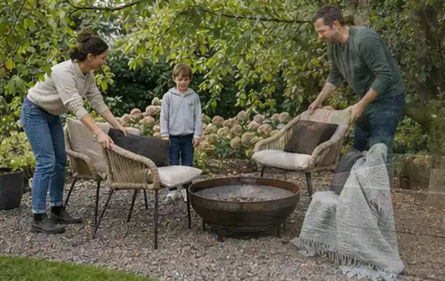 Familie stellt wetterfeste Sessel an einem geschützten Sitzplatz im Garten auf; Thema Pergolen, Schwerpunkt Kosten; Kontrolle.