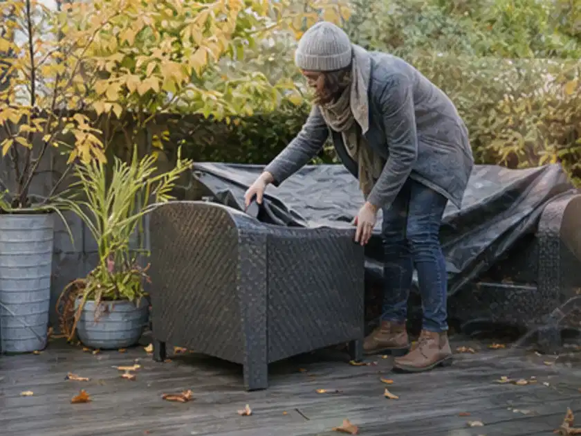 Person deckt Gartenmöbel vor der kalten Jahreszeit sorgfältig ab; Thema Pergolen, Schwerpunkt Winterlager; Titelbild.