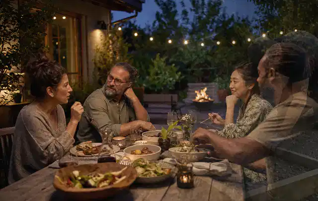 Menschen verbringen einen ruhigen Abend an einem Sitzplatz im Garten; Thema Pizzaöfen, Schwerpunkt Winterlager; Umsetzung.
