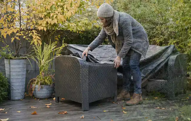 Person deckt Gartenmöbel vor der kalten Jahreszeit sorgfältig ab; Thema Poolabdeckungen, Schwerpunkt Checkliste; Kontrolle.
