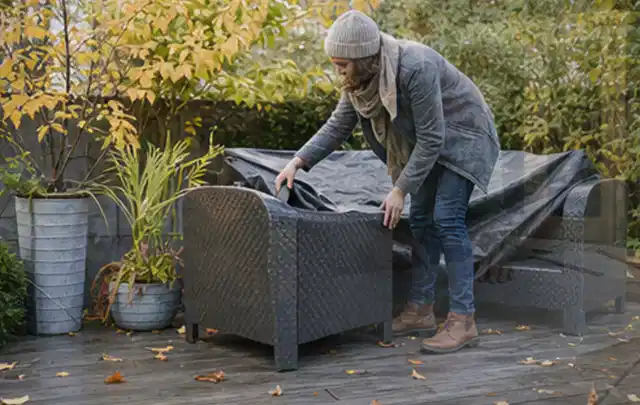 Person deckt Gartenmöbel vor der kalten Jahreszeit sorgfältig ab; Thema Poolabdeckungen, Schwerpunkt Gärten mit kleiner Fläche; Praxisalltag.