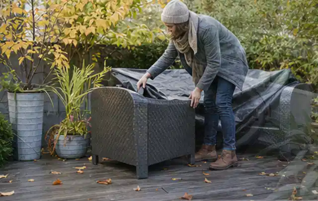 Person deckt Gartenmöbel vor der kalten Jahreszeit sorgfältig ab; Thema Poolabdeckungen, Schwerpunkt Kosten; Praxisalltag.