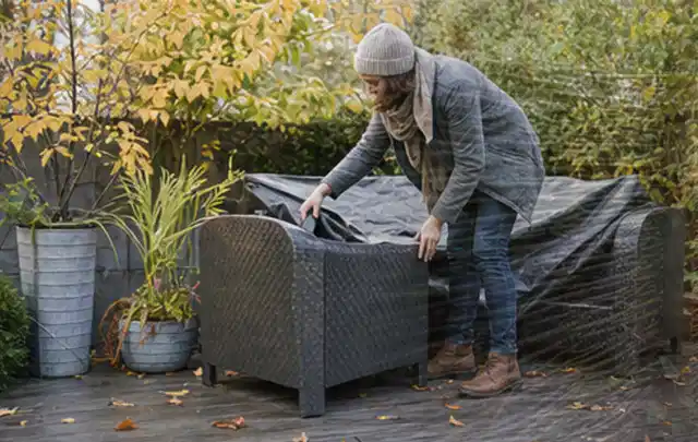 Person deckt Gartenmöbel vor der kalten Jahreszeit sorgfältig ab; Thema Poolabdeckungen, Schwerpunkt Reparatur; Praxisalltag.