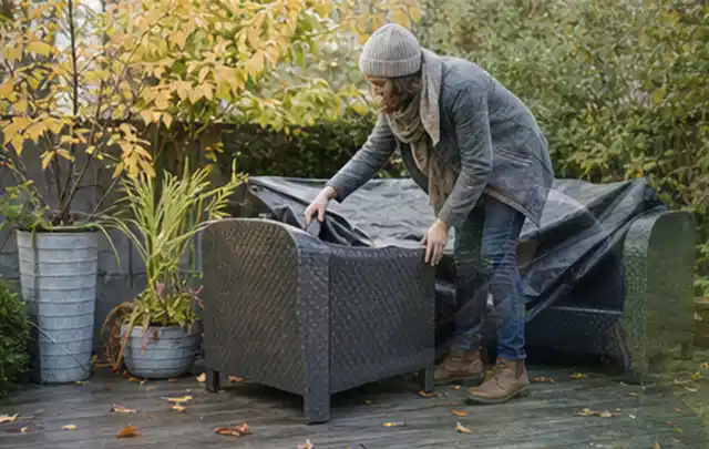Person deckt Gartenmöbel vor der kalten Jahreszeit sorgfältig ab; Thema Poolabdeckungen, Schwerpunkt Sicherheit; Kontrolle.