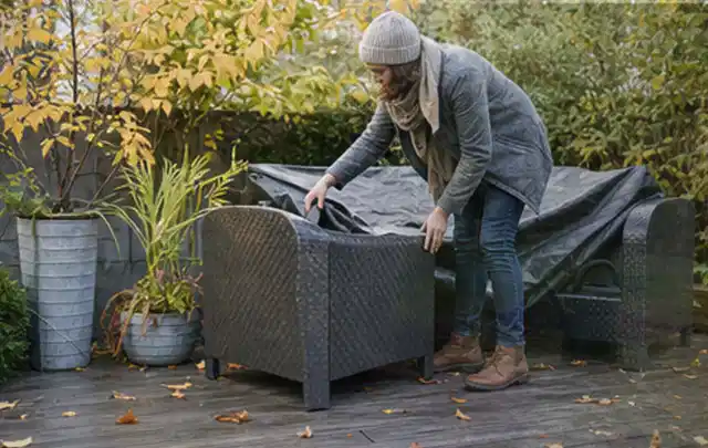 Person deckt Gartenmöbel vor der kalten Jahreszeit sorgfältig ab; Thema Poolabdeckungen, Schwerpunkt Vergleich; Praxisalltag.