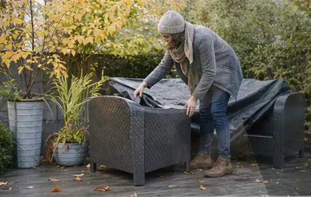Person deckt Gartenmöbel vor der kalten Jahreszeit sorgfältig ab; Thema Poolabdeckungen, Schwerpunkt Winterlager; Umsetzung.