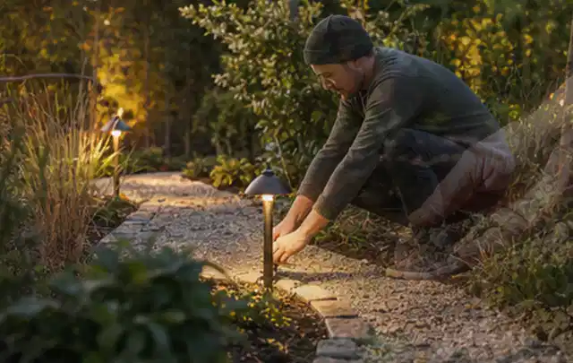 Person richtet eine niedrige warm leuchtende Gartenlampe am Kiesweg aus; Thema Poolchemie, Schwerpunkt Pools; Ausgangslage.