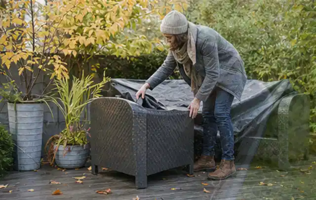 Person deckt Gartenmöbel vor der kalten Jahreszeit sorgfältig ab; Thema Poolfilter, Schwerpunkt Gärten mit kleiner Fläche; Praxisalltag.