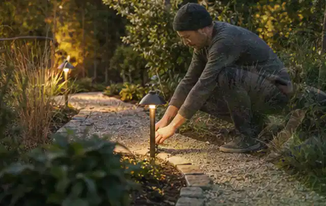 Person richtet eine niedrige warm leuchtende Gartenlampe am Kiesweg aus; Thema Poolfilter, Schwerpunkt Kaufberatung; Ergebnis.
