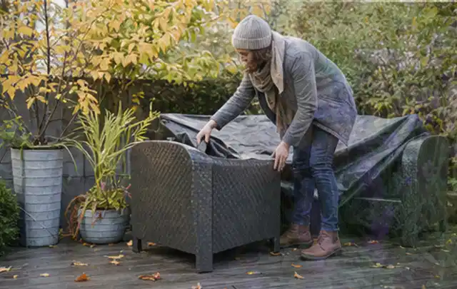 Person deckt Gartenmöbel vor der kalten Jahreszeit sorgfältig ab; Thema Poolfilter, Schwerpunkt Testkriterien; Praxisalltag.