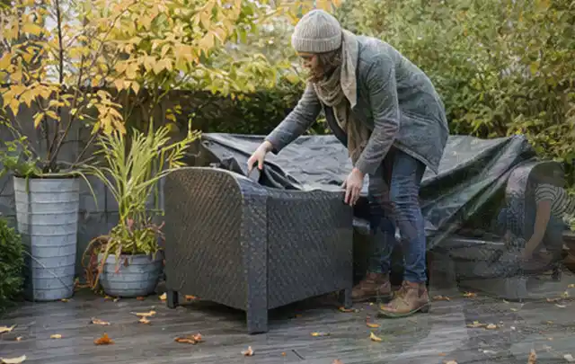 Person deckt Gartenmöbel vor der kalten Jahreszeit sorgfältig ab; Thema Poolfilter, Schwerpunkt Winterlager; Umsetzung.
