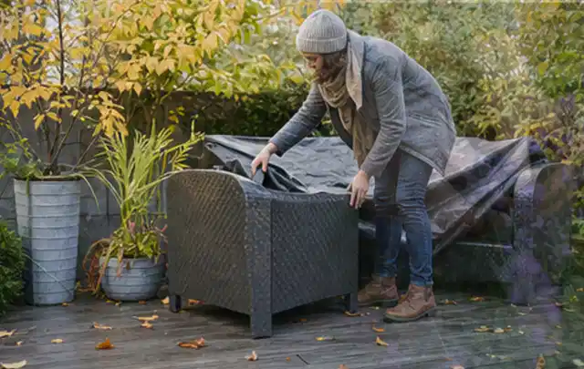 Person deckt Gartenmöbel vor der kalten Jahreszeit sorgfältig ab; Thema Poolheizungen, Schwerpunkt Reparatur; Ausgangslage.