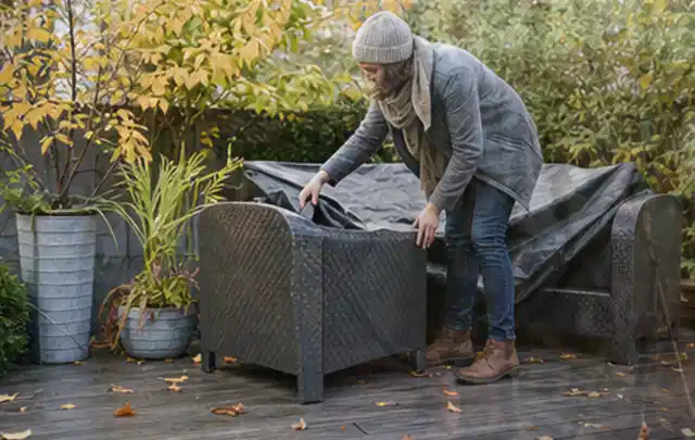 Person deckt Gartenmöbel vor der kalten Jahreszeit sorgfältig ab; Thema Poolpumpen, Schwerpunkt Systemvergleich; Praxisalltag.