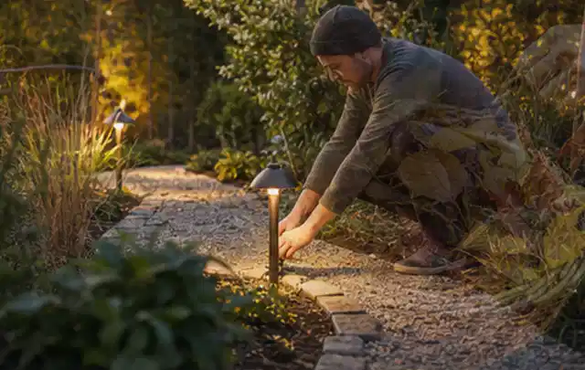 Person richtet eine niedrige warm leuchtende Gartenlampe am Kiesweg aus; Thema Poolpumpen, Schwerpunkt Testkriterien; Kontrolle.