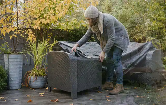 Person deckt Gartenmöbel vor der kalten Jahreszeit sorgfältig ab; Thema Poolroboter, Schwerpunkt Kosten; Praxisalltag.