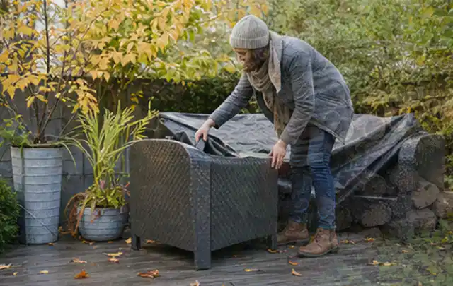 Person deckt Gartenmöbel vor der kalten Jahreszeit sorgfältig ab; Thema Poolroboter, Schwerpunkt Reparatur; Kontrolle.