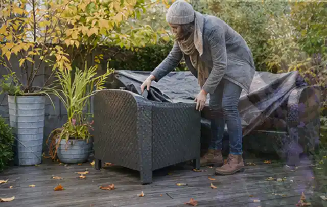 Person deckt Gartenmöbel vor der kalten Jahreszeit sorgfältig ab; Thema Poolroboter, Schwerpunkt Wartung; Kontrolle.
