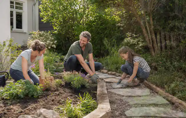Familie geht auf einem Weg durch einen abwechslungsreich gestalteten Garten; Thema Rankpflanzen als Sichtschutz, Schwerpunkt Baurecht; Ausgangslage.