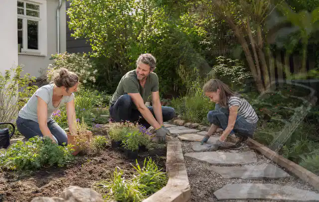Familie geht auf einem Weg durch einen abwechslungsreich gestalteten Garten; Thema Rankpflanzen als Sichtschutz, Schwerpunkt Kosten; Praxisalltag.