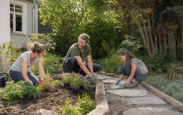 Familie geht auf einem Weg durch einen abwechslungsreich gestalteten Garten; Thema Rankpflanzen als Sichtschutz, Schwerpunkt Materialwahl; Ergebnis.