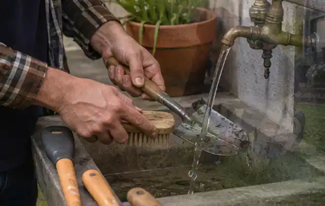 Hände reinigen gebrauchte Gartengeräte mit Bürste und Wasser am Außenbecken; Thema Rasenmäher, Schwerpunkt Gärten mit kleiner Fläche; Ergebnis.