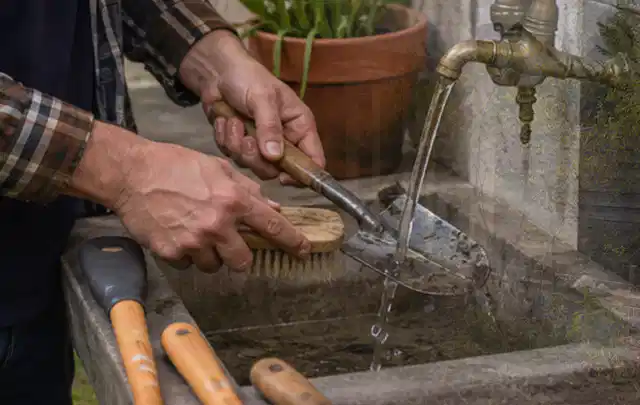 Hände reinigen gebrauchte Gartengeräte mit Bürste und Wasser am Außenbecken; Thema Rasenmäher, Schwerpunkt Gartengeräte; Ergebnis.