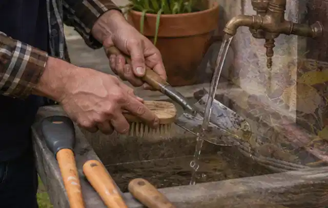 Hände reinigen gebrauchte Gartengeräte mit Bürste und Wasser am Außenbecken; Thema Rasenmäher, Schwerpunkt Kaufberatung; Umsetzung.
