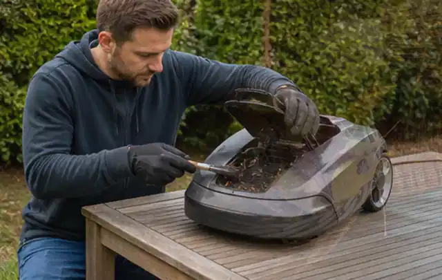 Person wartet einen geöffneten Mähroboter auf einem stabilen Gartentisch; Thema Rasenmäher, Schwerpunkt Kosten; Ausgangslage.