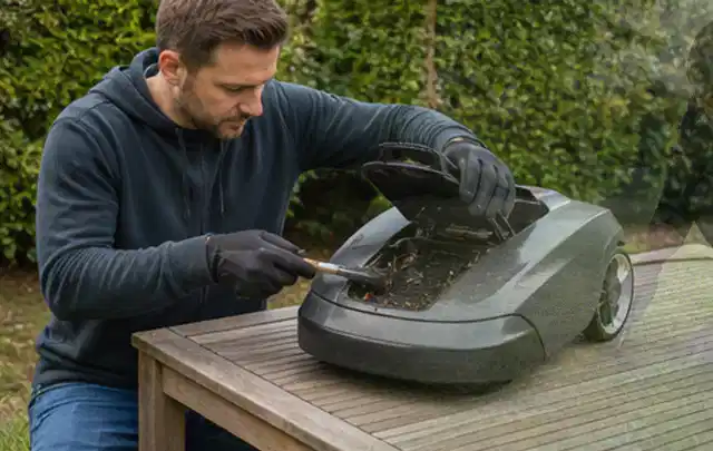 Person wartet einen geöffneten Mähroboter auf einem stabilen Gartentisch; Thema Rasenmäher, Schwerpunkt Testkriterien; Kontrolle.