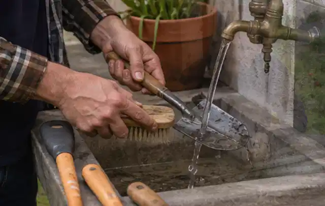 Hände reinigen gebrauchte Gartengeräte mit Bürste und Wasser am Außenbecken; Thema Rasenmäher, Schwerpunkt Vergleich; Praxisalltag.