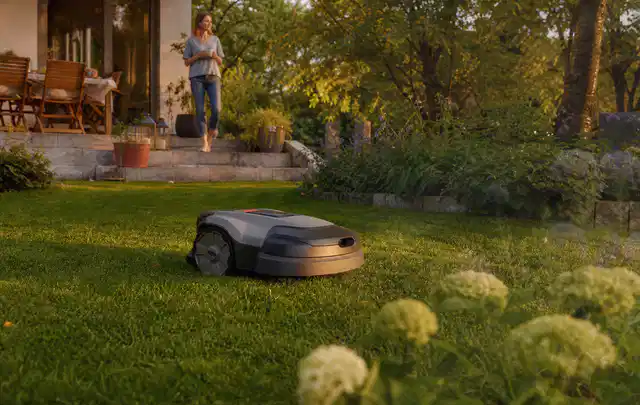 Mähroboter fährt am Abend über einen Rasen im Familiengarten; Thema RTK Mähroboter, Schwerpunkt Checkliste; Praxisalltag.