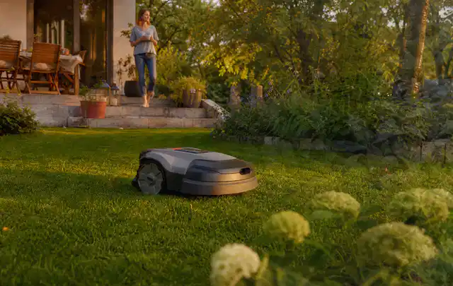 Mähroboter fährt am Abend über einen Rasen im Familiengarten; Thema Segway Navimow, Schwerpunkt Anwendung; Kontrolle.