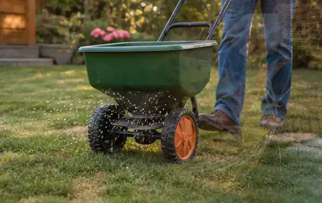 Person verteilt Rasensamen mit einem Streuwagen auf einer lückigen Fläche; Thema Segway Navimow, Schwerpunkt Nachhaltigkeit; Kontrolle.