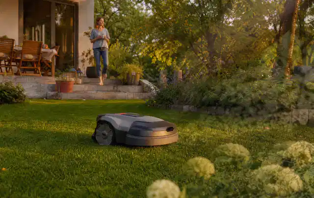 Mähroboter fährt am Abend über einen Rasen im Familiengarten; Thema Segway Navimow, Schwerpunkt Reinigung; Umsetzung.
