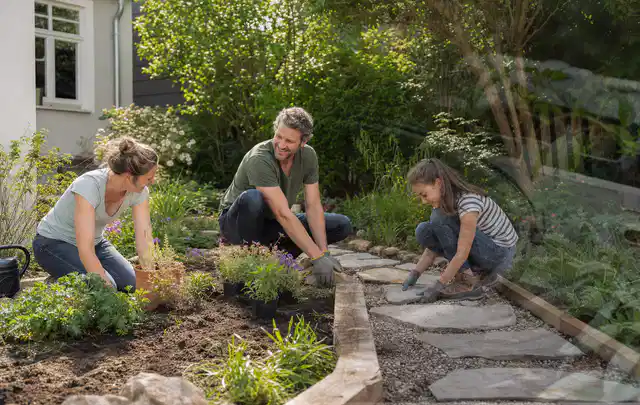 Familie geht auf einem Weg durch einen abwechslungsreich gestalteten Garten; Thema Sichtschutz aus Holz, Schwerpunkt Dimensionierung; Umsetzung.