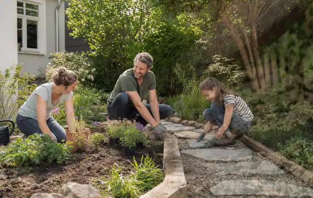 Familie geht auf einem Weg durch einen abwechslungsreich gestalteten Garten; Thema Sichtschutzhecken, Schwerpunkt Kosten; Praxisalltag.