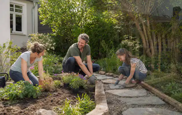 Familie geht auf einem Weg durch einen abwechslungsreich gestalteten Garten; Thema Sichtschutzmatten, Schwerpunkt Fundament; Kontrolle.