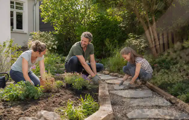 Familie geht auf einem Weg durch einen abwechslungsreich gestalteten Garten; Thema Sichtschutzmatten, Schwerpunkt Gestaltung; Praxisalltag.