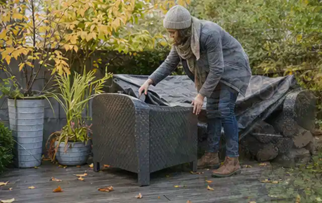 Person deckt Gartenmöbel vor der kalten Jahreszeit sorgfältig ab; Thema Smoker, Schwerpunkt Wartung; Kontrolle.