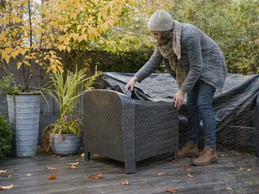 Person deckt Gartenmöbel vor der kalten Jahreszeit sorgfältig ab; Thema Smoker, Schwerpunkt Winterlager; Titelbild.